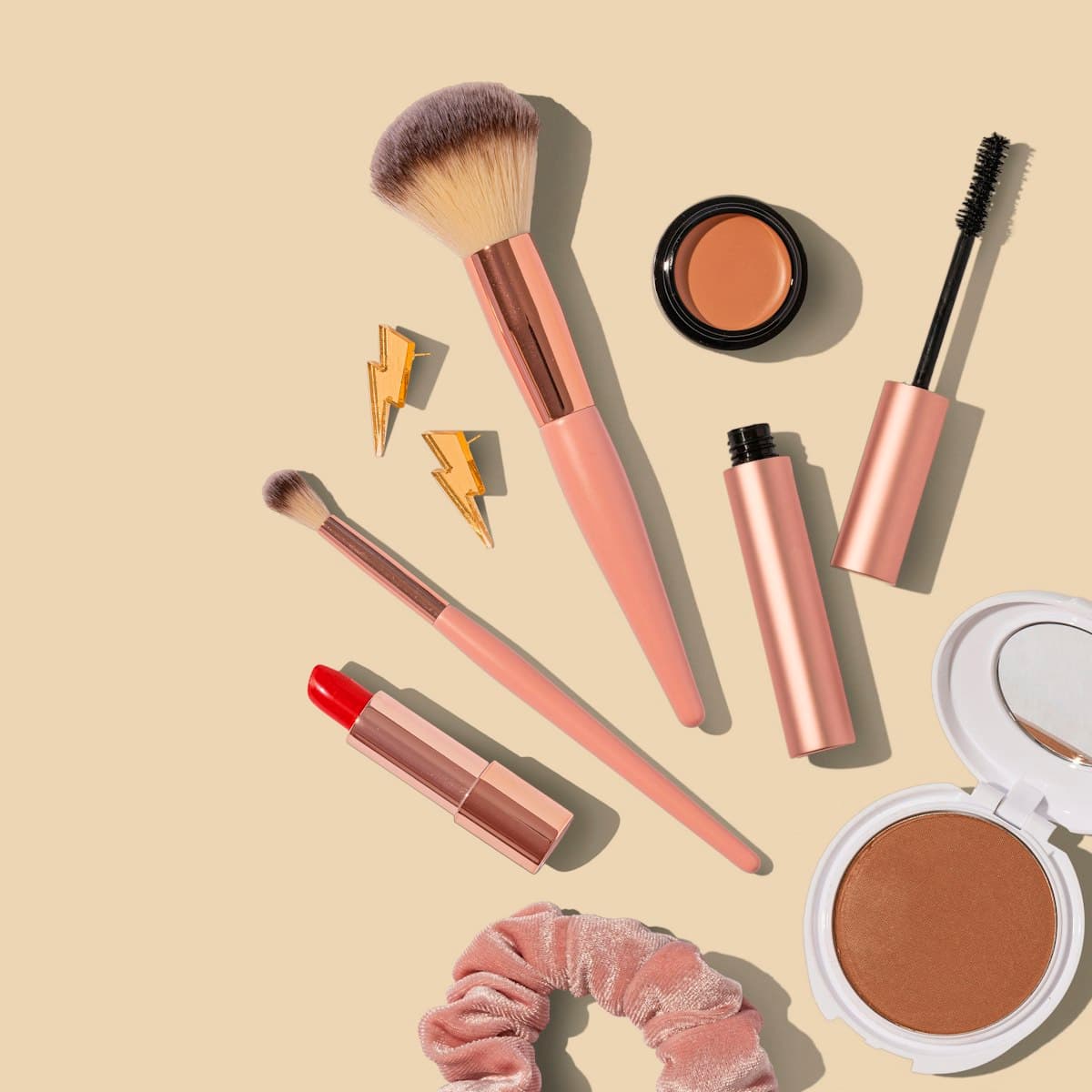 Brushes, lipstick and bronzer laid out on a peach backdrop