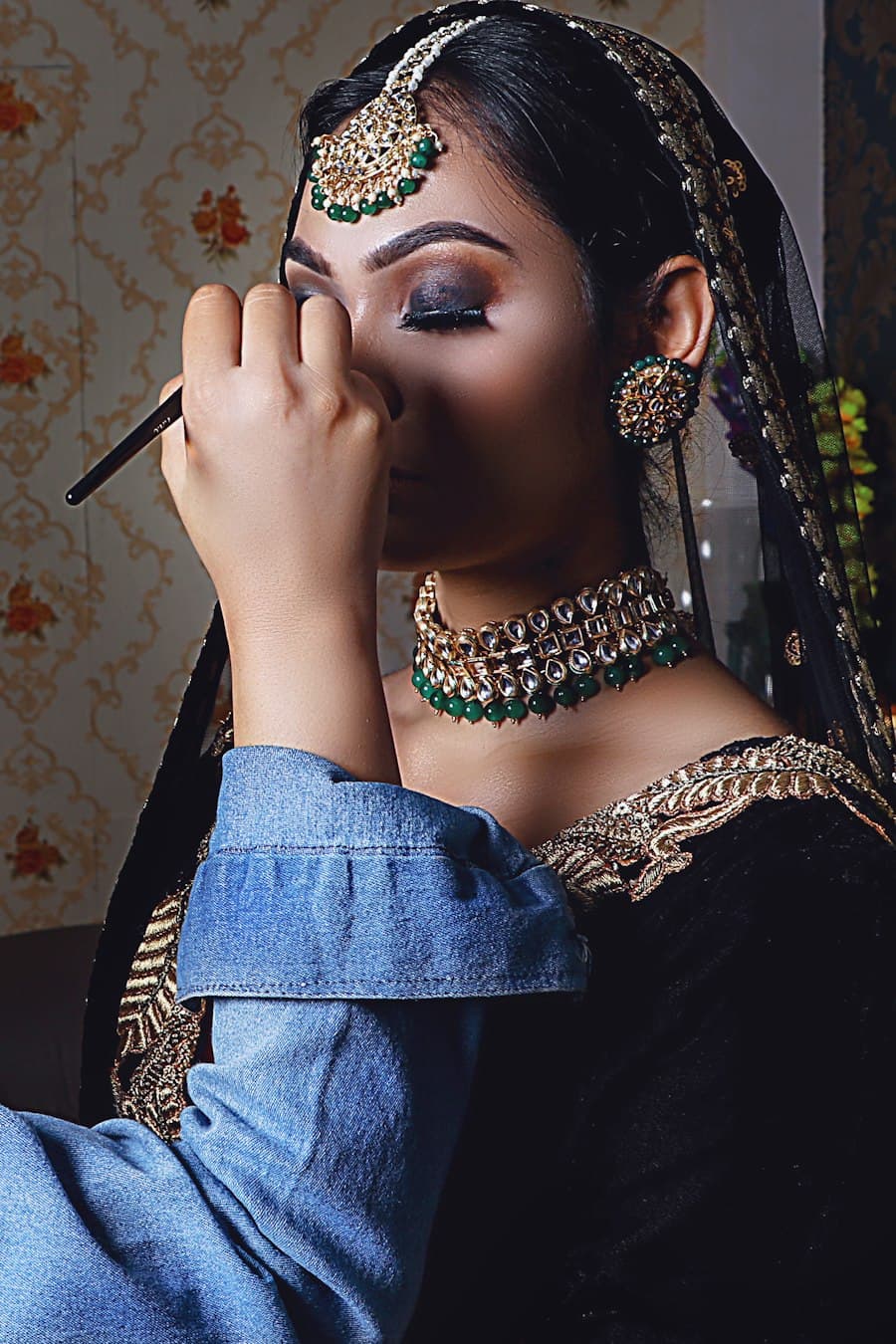 A bride having her eye makeup done, in gold jewellery and dupatta